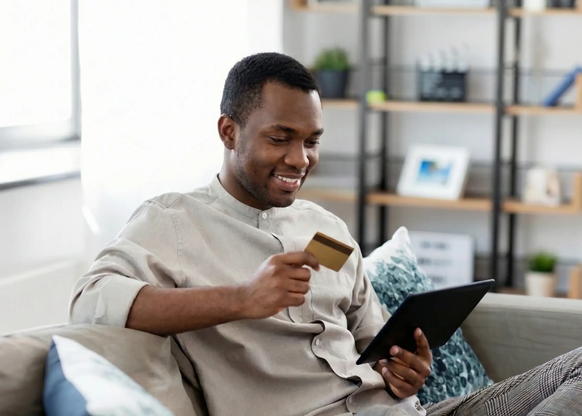 A person sitting on a couch using a tablet while holding a credit card to learn how to build credit with a credit card 2025.